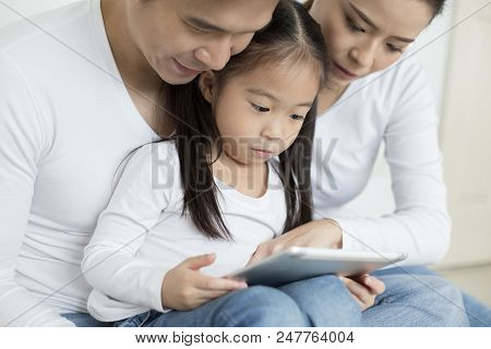 Little Girl Using Tablet With Dad And Mon Together At Home. People With Technology Concept.