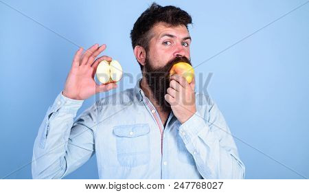 Man Bearded Eats Fruit, Holds Apple Blue Background. Half Of Apple Healthy Lifestyle. Nutritional Va
