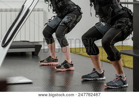 Young Athletic Women In Ems Suits Exercising In Modern Gym