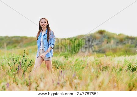 Happy Smiling Young Girl Wearing Blue Jeans Jacket And Shorts Is Standing In The Field