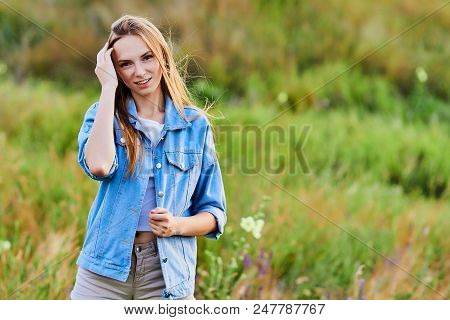 Happy Smiling Young Girl Wearing Blue Jeans Jacket And Shorts Is Standing In The Field
