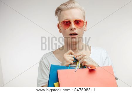 Amased Albino Young Man Wearing White T-shirt, Posing With Coloful Shopping Bags Over Studio White B