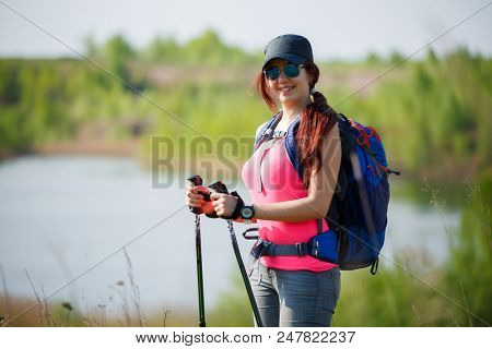 Picture of sporty woman with walking sticks on background of lake and green vegetation