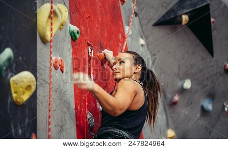 Beautiful Young Strong Woman Climbing On Rock Artificial Wall Top View. Female Climber Insured On Be