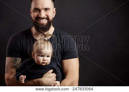 Father And Infant Daughter Posing With Different Grimaces At Studio Black Background Witj Copyspace.