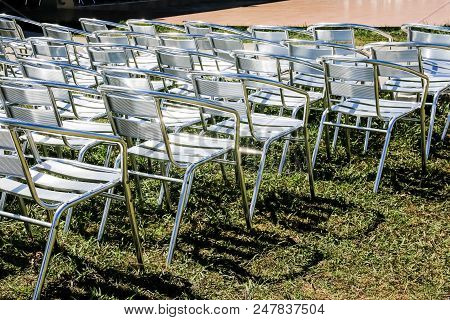 Symmetrical Rows Of Silver Folding Chairs With A Green Folder Placed On The Seat Of Each One