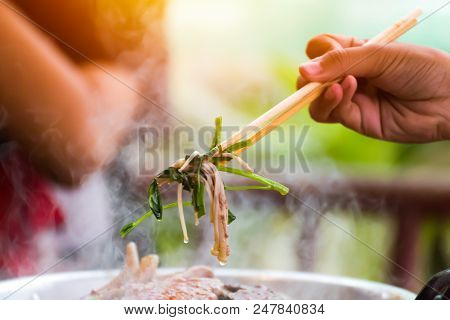 People cooking meat and grill. Food are vegeteble. People use chopsticks.