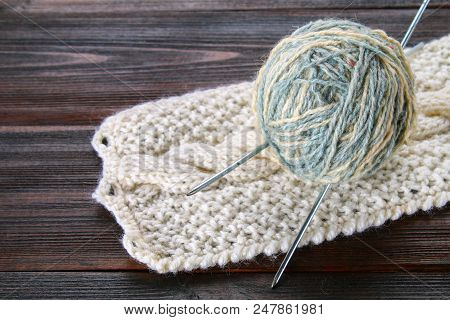A Ball Of Wool With Knitting Needles And Knitted Socks On A Wooden Table. Needlework