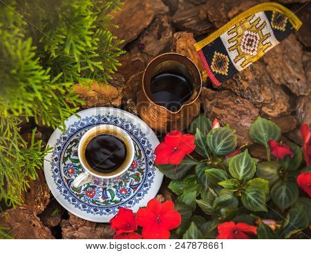 A Coffee Cup With Saucer And Jezva Stand Among The Bark, Flowers And Branches Of Cypress. Top View