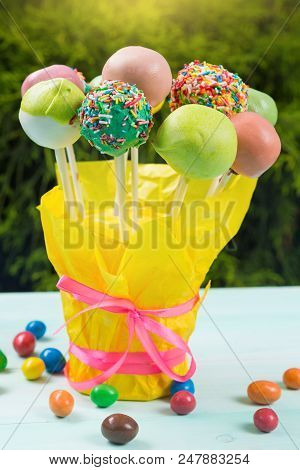 A Lot Of Colored Pop Cakes In A Glass On Turquoise Boards, In The Open Air, Against A Background Of 