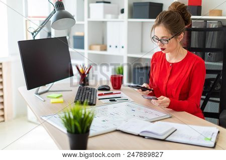 Beautiful Young Girl In Glasses And A Red Shirt Is Working In The Office. Photo With Depth Of Field.
