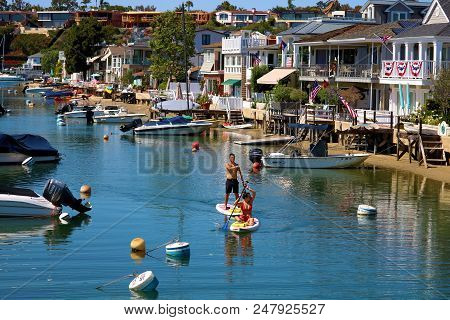 July 2, 2018 In Newport Beach, Ca:  People Paddle Boarding At A Canal Surrounded By Residential Home
