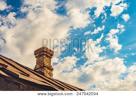 An Old Brick Pipe On The Roof Of A Residential Building With An Iron Roof Against A Background Of Cl