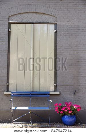 Bench And A Vase Of Flowers In Front Of A Window With Closed Shutters In The Brabant Village Of Drim