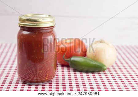 Salsa On A Red Gingham Table Cloth In A Home Canning Jar