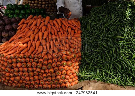 An Indian Man Is Selling Fresh Indian Vegetables From His Market Stall. There Are Kakdi Cuccumbers, 