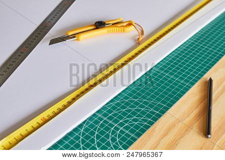 Cutter, Ruller And Pencil On A Green Mat And Wooden Table Background