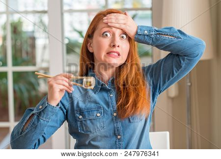 Redhead woman eating sushi using chopsticks stressed with hand on head, shocked with shame and surprise face, angry and frustrated. Fear and upset for mistake.