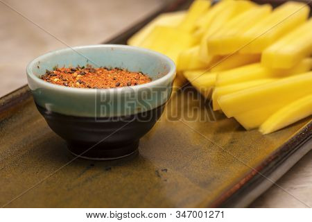Small Bowl Of Seasonings Used To Make Sushi And Julienne Cut Mango On A Ceramic Plate