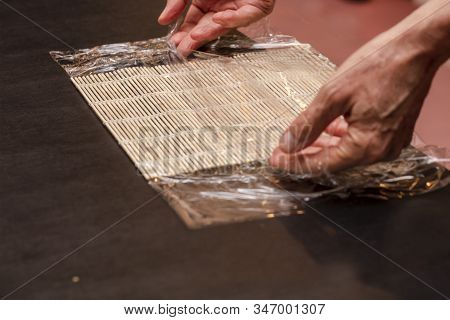 Chef Preparing Sushi Mat With Plastic Wrap To Make A Roll For A Cooking Class