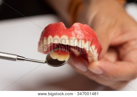 Denture prosthesis in doctor orthodentist dentist hand, checking with mirror