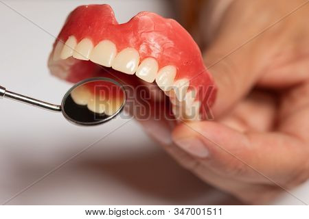 Denture prosthesis in doctor orthodentist dentist hand, checking with mirror