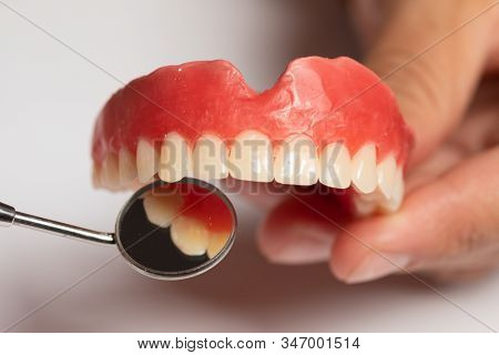 Denture prosthesis in doctor orthodentist dentist hand, checking with mirror