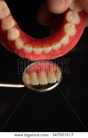 Denture prosthesis in doctor orthodentist dentist hand, checking with mirror