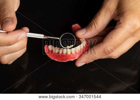 Denture prosthesis in doctor orthodentist dentist hand, checking with mirror