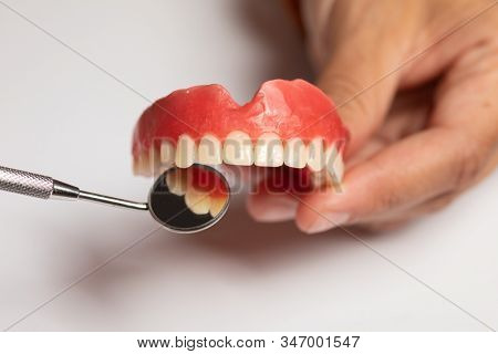 Denture prosthesis in doctor orthodentist dentist hand, checking with mirror