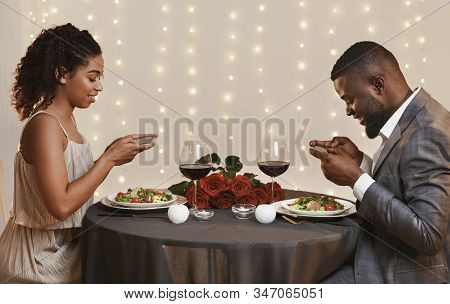 Black Couple Taking Photos Of Meal While Having Dinner In Restaurant, Celebrating St. Valentines Day