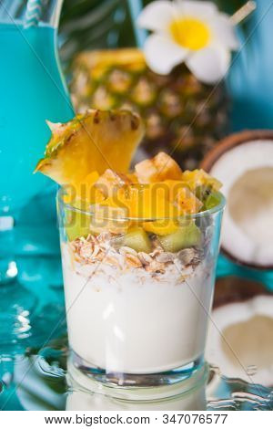Exotic Tropical Fruit Salad With Muesli And Yogurt In A Glass With Pineapple And Coconut On The Back