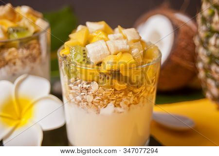 Exotic Tropical Fruit Salad With Muesli And Yogurt In A Glass With Pineapple And Coconut On The Back