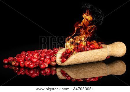 Peruvian Pink Pepper With Burning Fire In Scoop Isolated On Black Glass