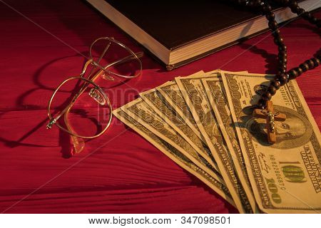 Rosary Beads, Money, Glasses And Holy Bible. Church Donation Or Tithe Concept. Red Wood Table Surfac