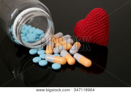 Pills And Knitted Red Heart On Dark Glass Table, Bottle With Medication In Capsules. Concept Of Hype