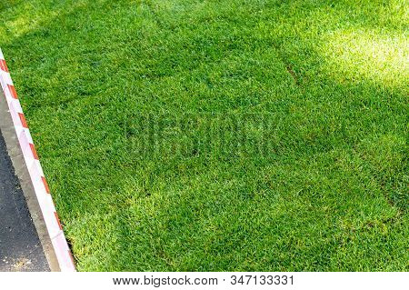 Straigh Line Of New Freshly Installed Green Rolled Lawn Grass Carpet Along Stone Pavement Sidewalk A