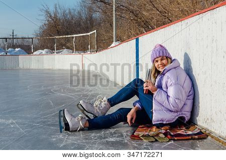 Lovely Young Woman Relaxing After Riding Ice Skates And Drinking Hot Drink From Termo Pot On The Ice