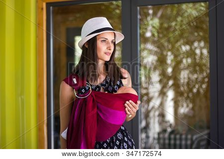 Almaty, Kazakhstan - July 08, 2019: Young Beautiful Babywearing Mother Carry Her Newborn Baby In A R