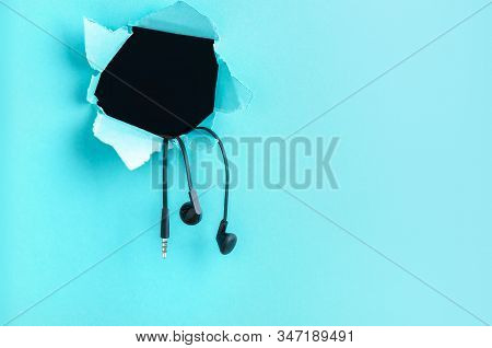 Headphones Hang From A Hole In The Paper On A Blue Background