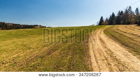 Springtime Meadow With Dirty Road, Forest Around And Clear Sky Above Near Vrchrieka Hill In Javornik