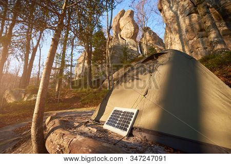 Small Solar Panel And Tourist Tent In The Forest At The Foot Of The Cliffs. Fir Trees And Fallen Lea