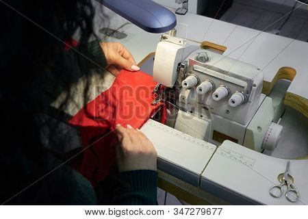 Young Woman Using Professional Overlock Sewing Machine In Workshop Studio. Equipment For Edging, Hem