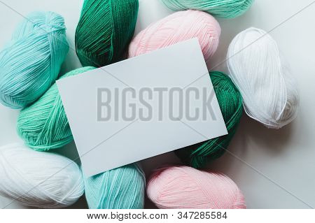 White Paper Sheet On Acrylic Soft Pastel Colored Wool Yarn Thread Skeins Heap On White Background, T