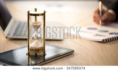 Time Is Running In Hourglass, Female Manager Checking Graphs At Office Desk