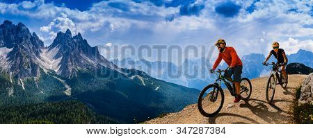 Cycling woman and man riding on bikes in Dolomites mountains andscape. Couple cycling MTB enduro trail track. Outdoor sport activity.
