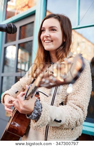 Female Musician Busking Playing Acoustic Guitar And Singing Outdoors In Street