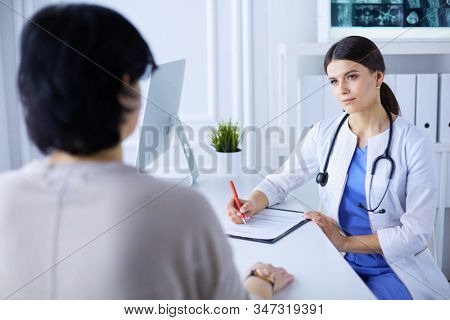 Doctor and patient discussing medical problems in a hospital consulting room. Doc filling in a patient's form