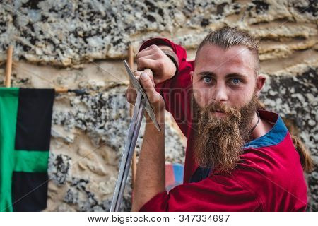 A Bearded Viking Brandishing A Steel Broadsword Looking At The Camera