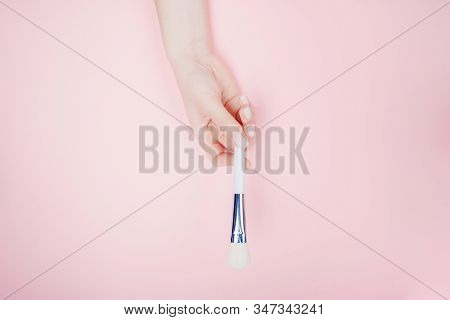 Girl Hand Hold White Brushes Makeup On Pink Color Background. Top View Flat Lay
